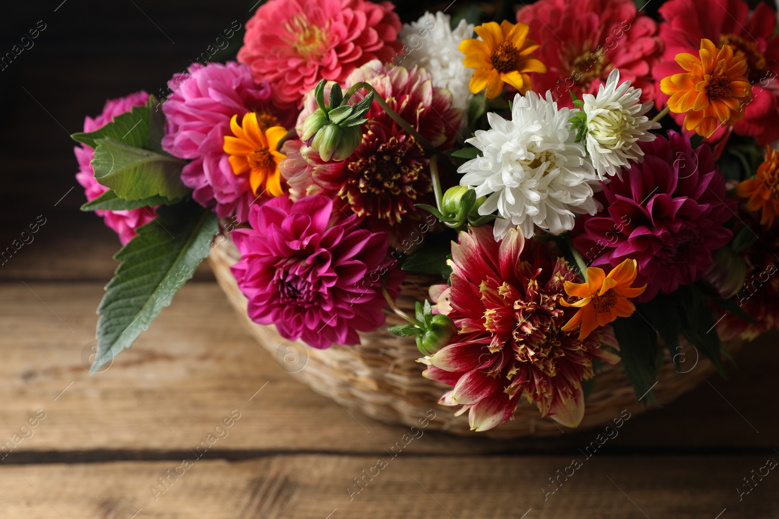 Photo of Beautiful wild flowers and leaves in wicker basket on wooden table, closeup