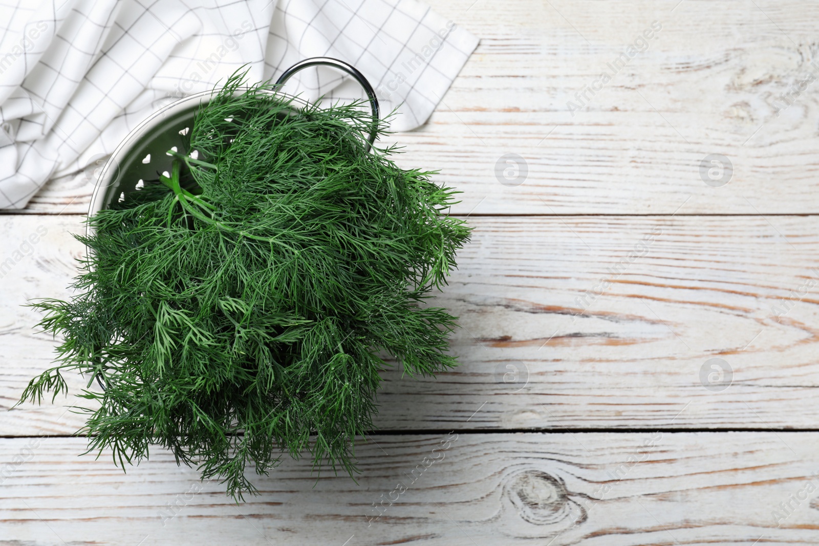 Photo of Fresh dill in colander on white wooden table, top view. Space for text