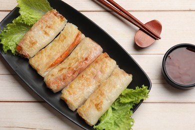 Photo of Delicious fried spring rolls, sauce and chopsticks on light wooden table, flat lay