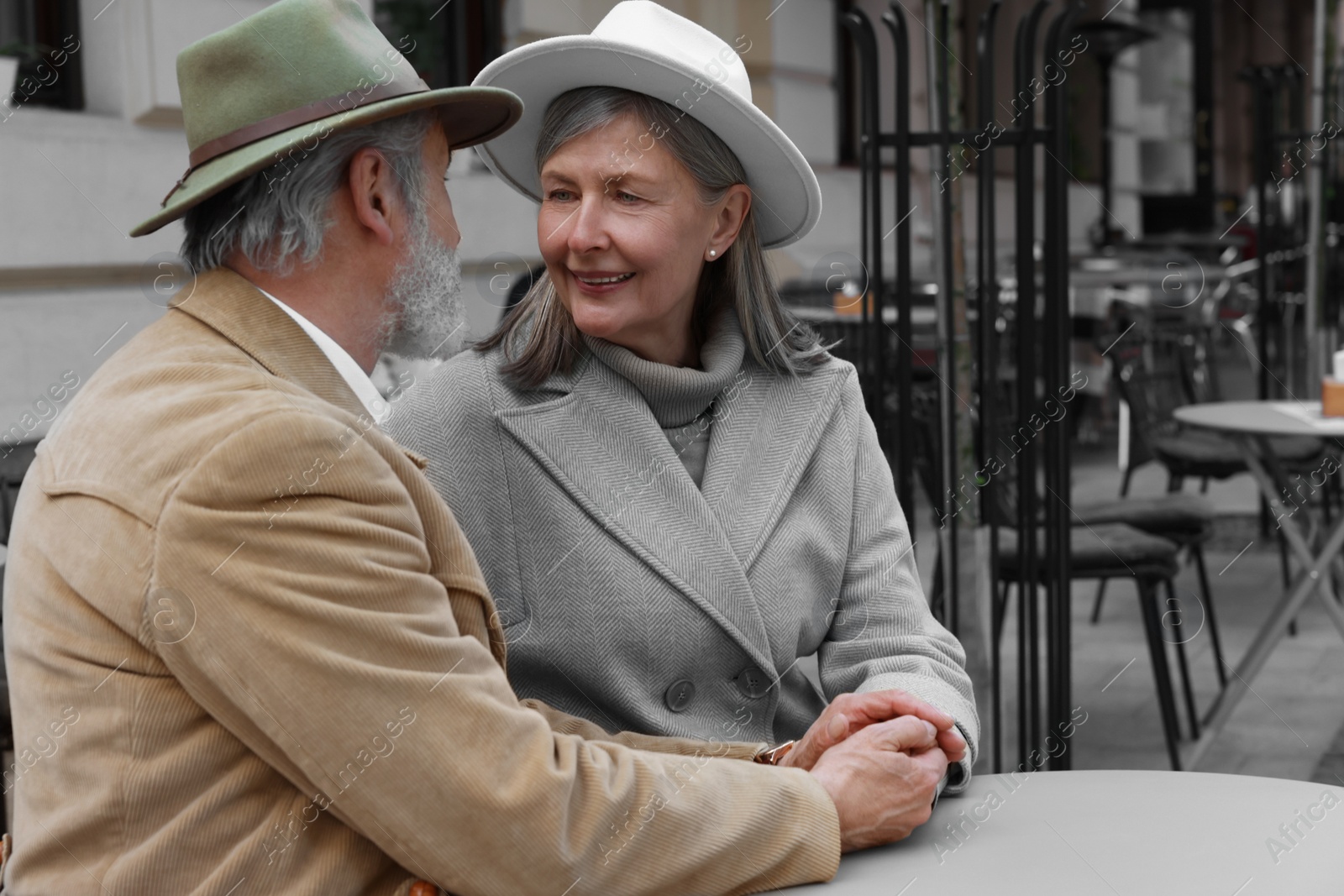 Photo of Portrait of affectionate senior couple sitting in outdoor cafe, space for text