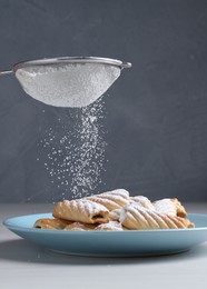 Photo of Woman with sieve sprinkling powdered sugar onto cookies at white wooden table, closeup