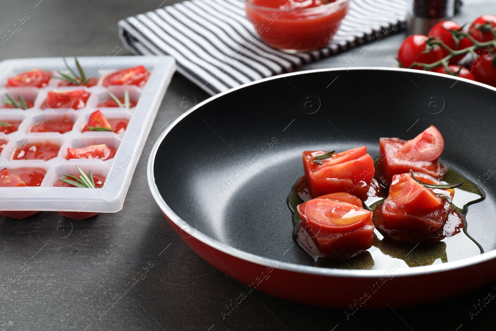 Photo of Melting ice cubes with tomatoes, oil and rosemary on grey table