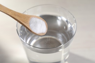 Photo of Adding baking soda into glass of water on light background, closeup