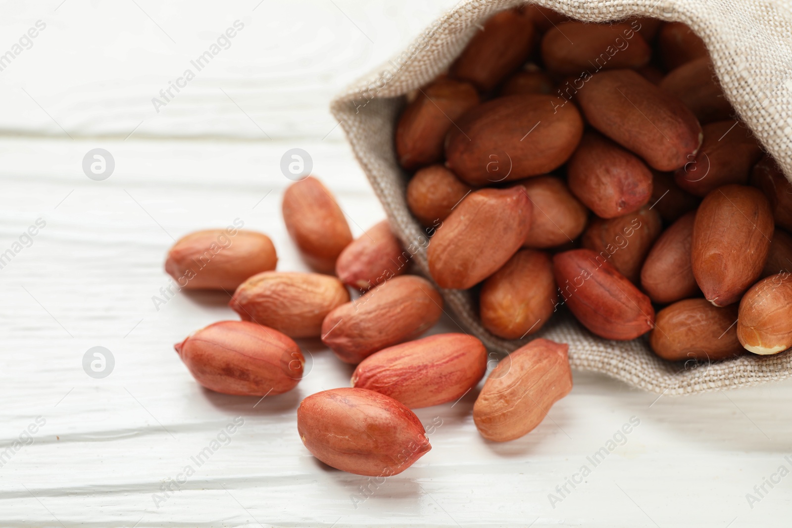 Photo of Fresh peanuts in sack on white wooden table, closeup