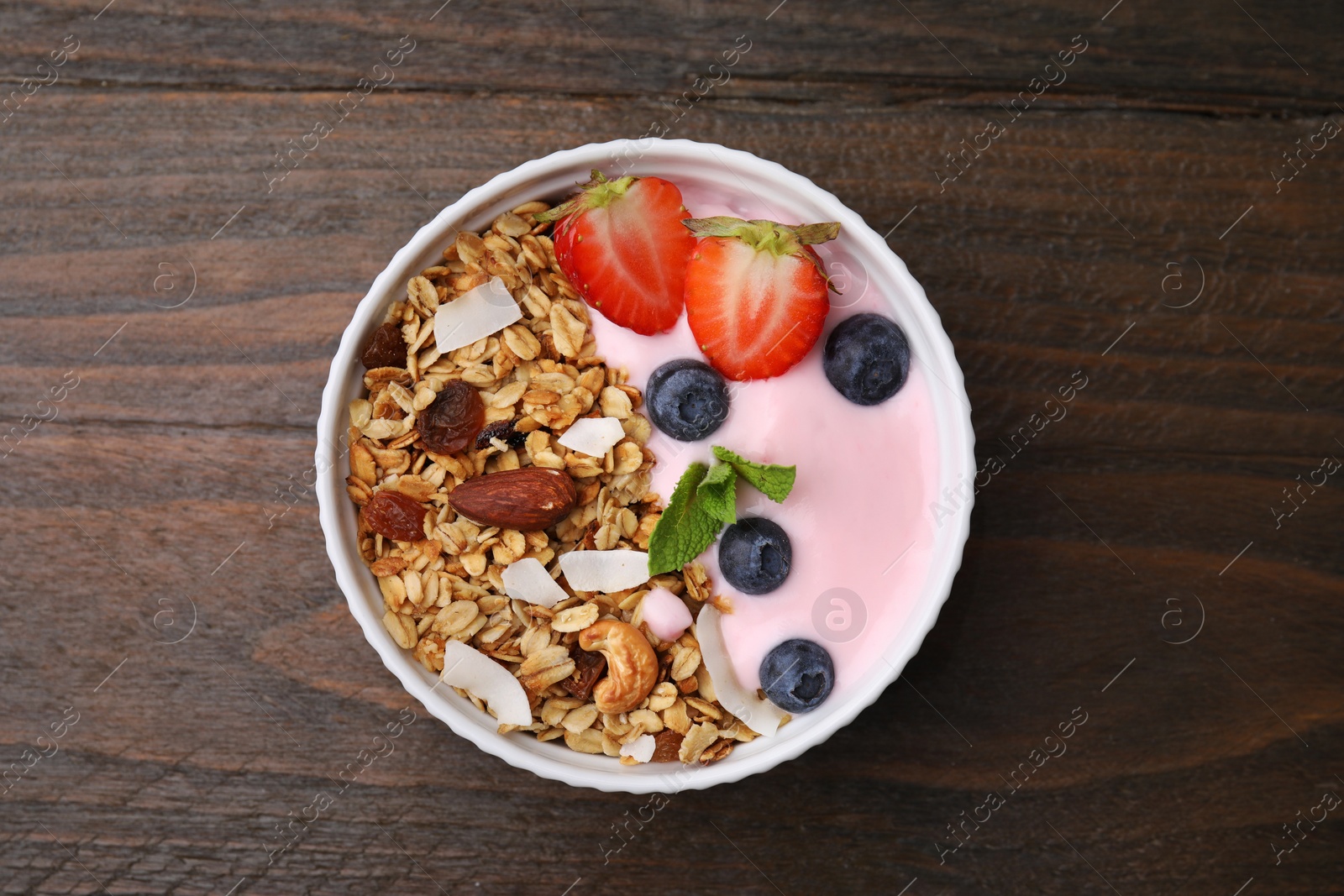 Photo of Tasty granola, yogurt and fresh berries in bowl on wooden table, top view. Healthy breakfast