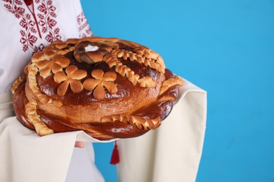 Photo of Woman with korovai on light blue background, closeup. Ukrainian bread and salt welcoming tradition