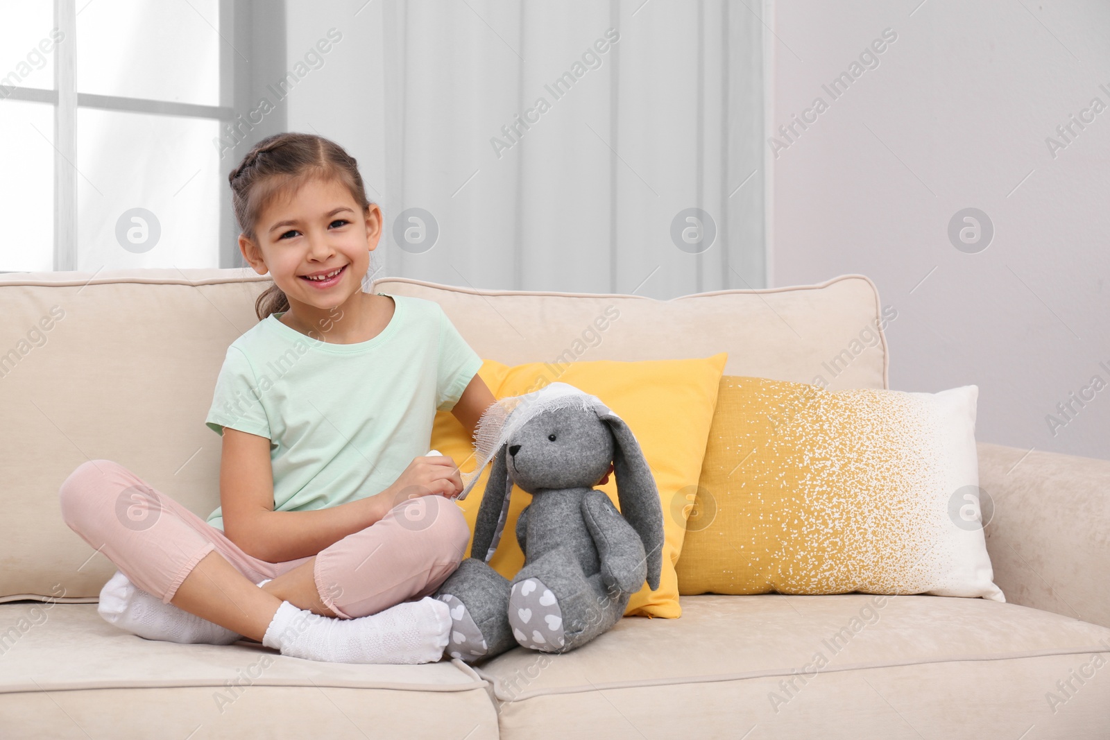 Photo of Cute child playing doctor with stuffed toy on sofa in hospital