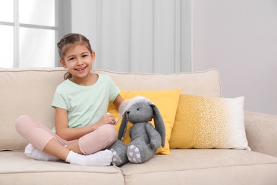 Photo of Cute child playing doctor with stuffed toy on sofa in hospital