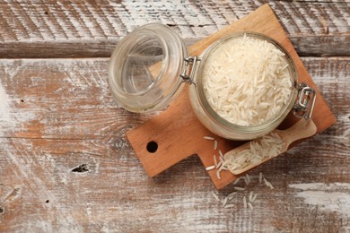 Photo of Raw basmati rice in jar and scoop on wooden table, top view. Space for text