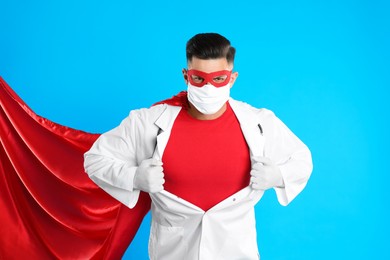 Photo of Doctor wearing face mask and cape on light blue background. Super hero power for medicine