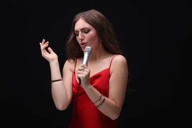 Photo of Beautiful woman with microphone singing on black background