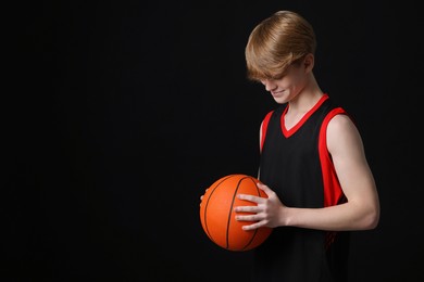 Photo of Teenage boy with basketball ball on black background. Space for text