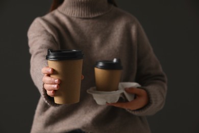 Photo of Woman holding takeaway cardboard cups on black background, closeup. Coffee to go