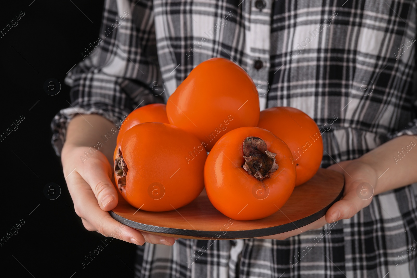 Photo of Woman holding delicious ripe juicy persimmons on black background, closeup