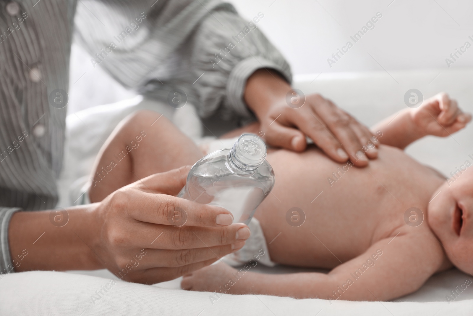 Photo of Mother massaging her baby with oil on changing table indoors, closeup