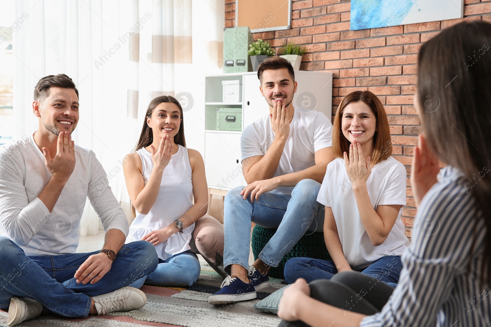 Photo of Group of young people learning sign language with teacher indoors