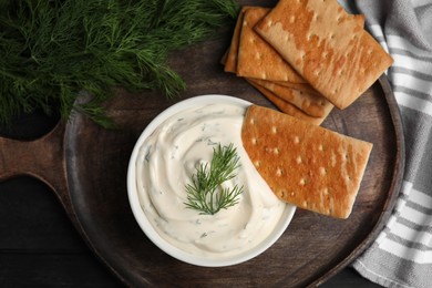 Tasty creamy dill sauce with crackers on wooden table, flat lay