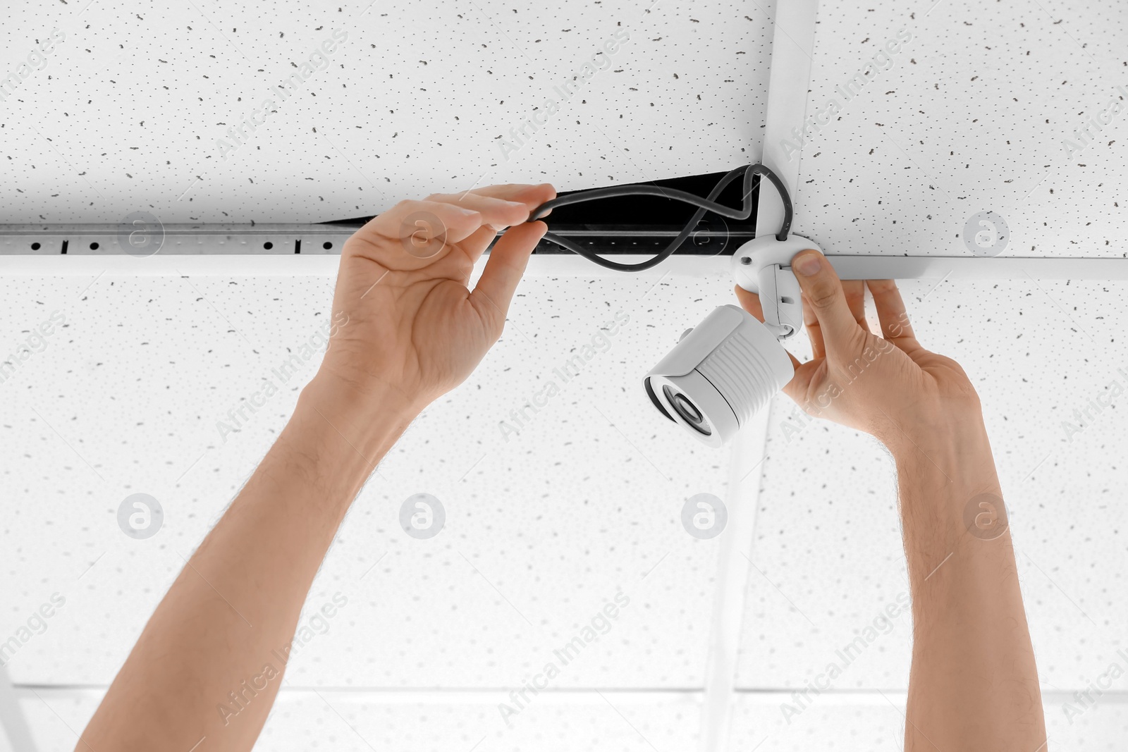 Photo of Technician installing CCTV camera on ceiling indoors, closeup