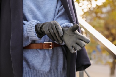 Young woman putting on stylish black leather gloves outdoors, closeup