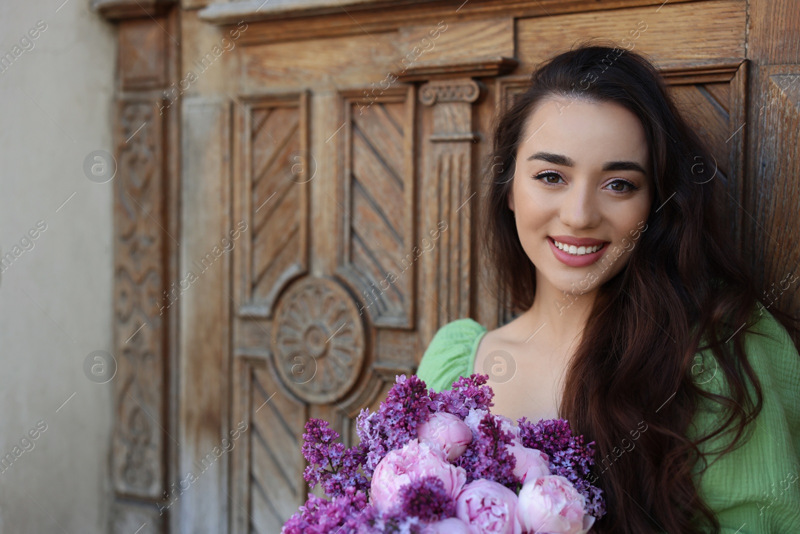 Photo of Beautiful woman with bouquet of spring flowers near wooden door, space for text