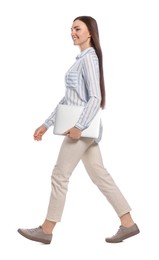 Young woman with laptop walking on white background