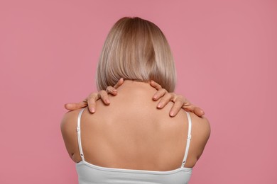 Photo of Woman suffering from pain in her neck on pink background, back view