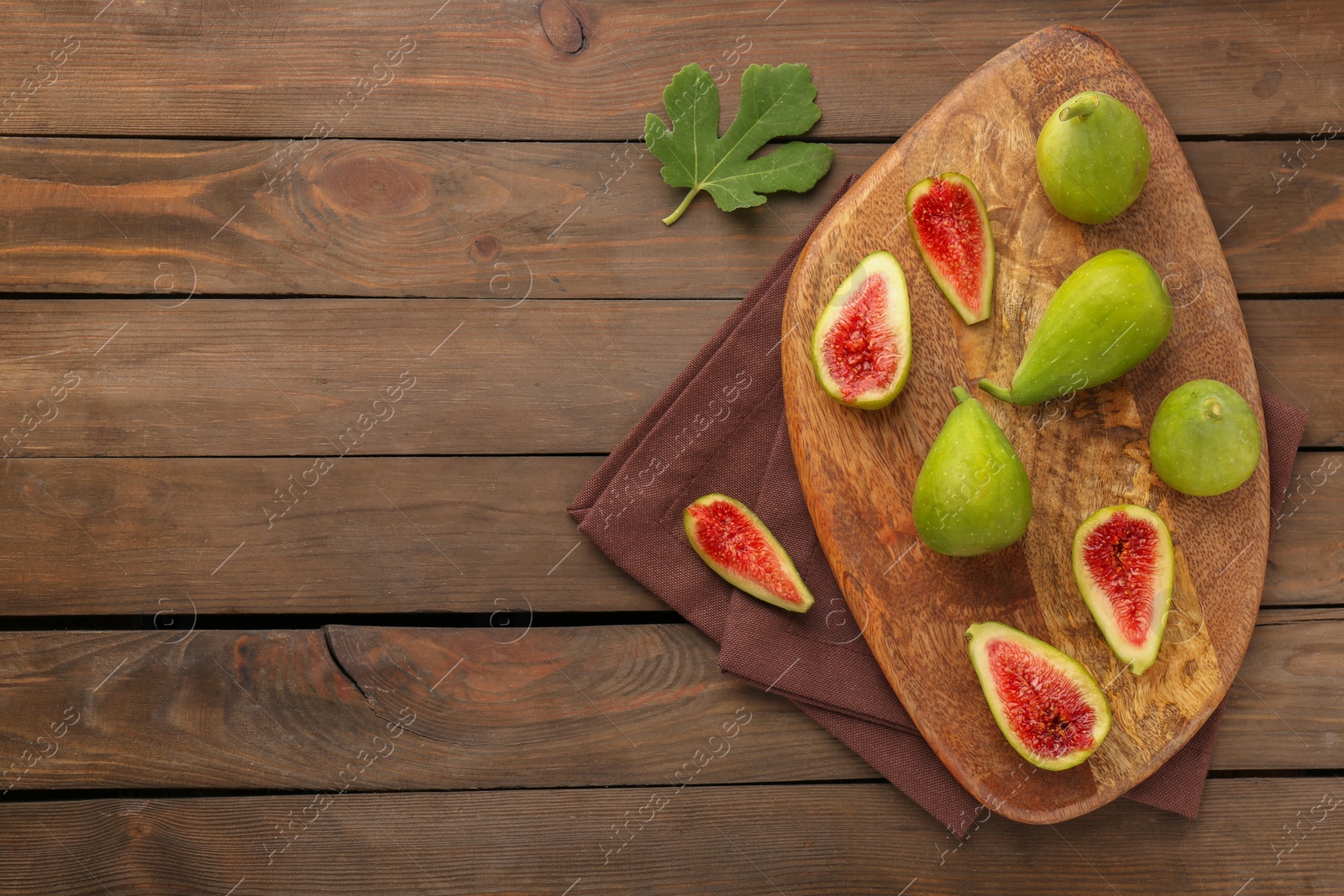 Photo of Cut and whole green figs on wooden table, flat lay. Space for text