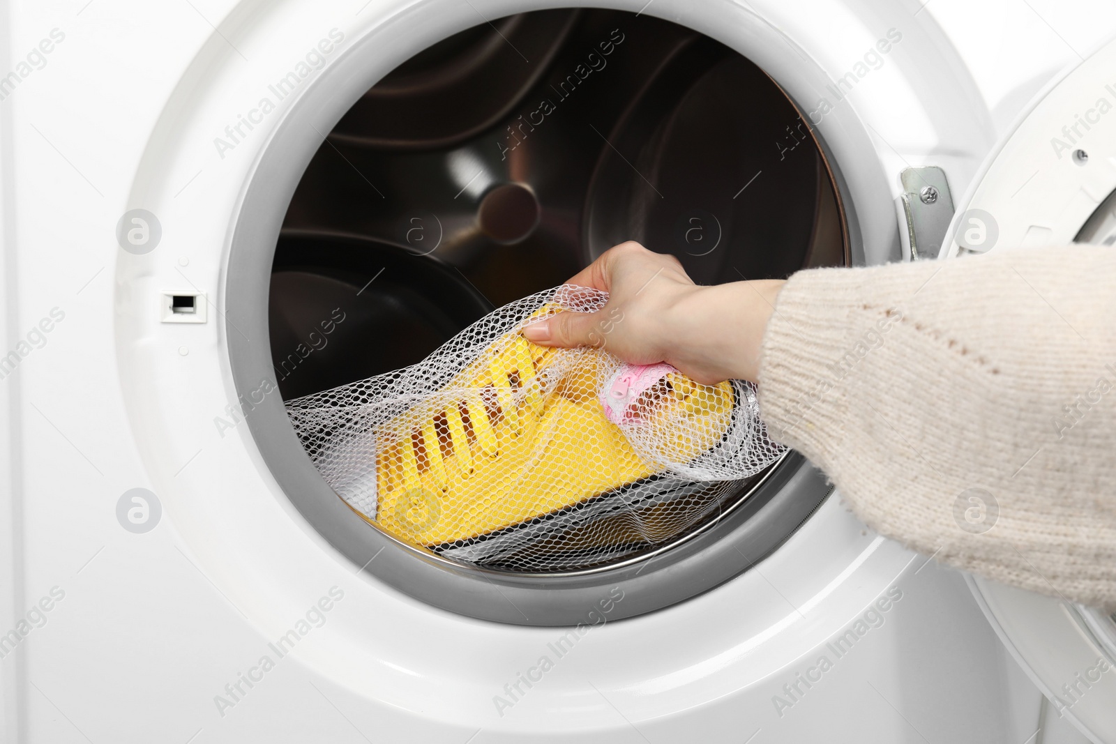 Photo of Woman putting stylish sneakers into washing machine, closeup