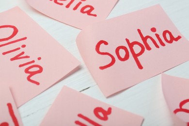 Photo of Paper stickers with different names on white wooden table, closeup. Choosing baby's name
