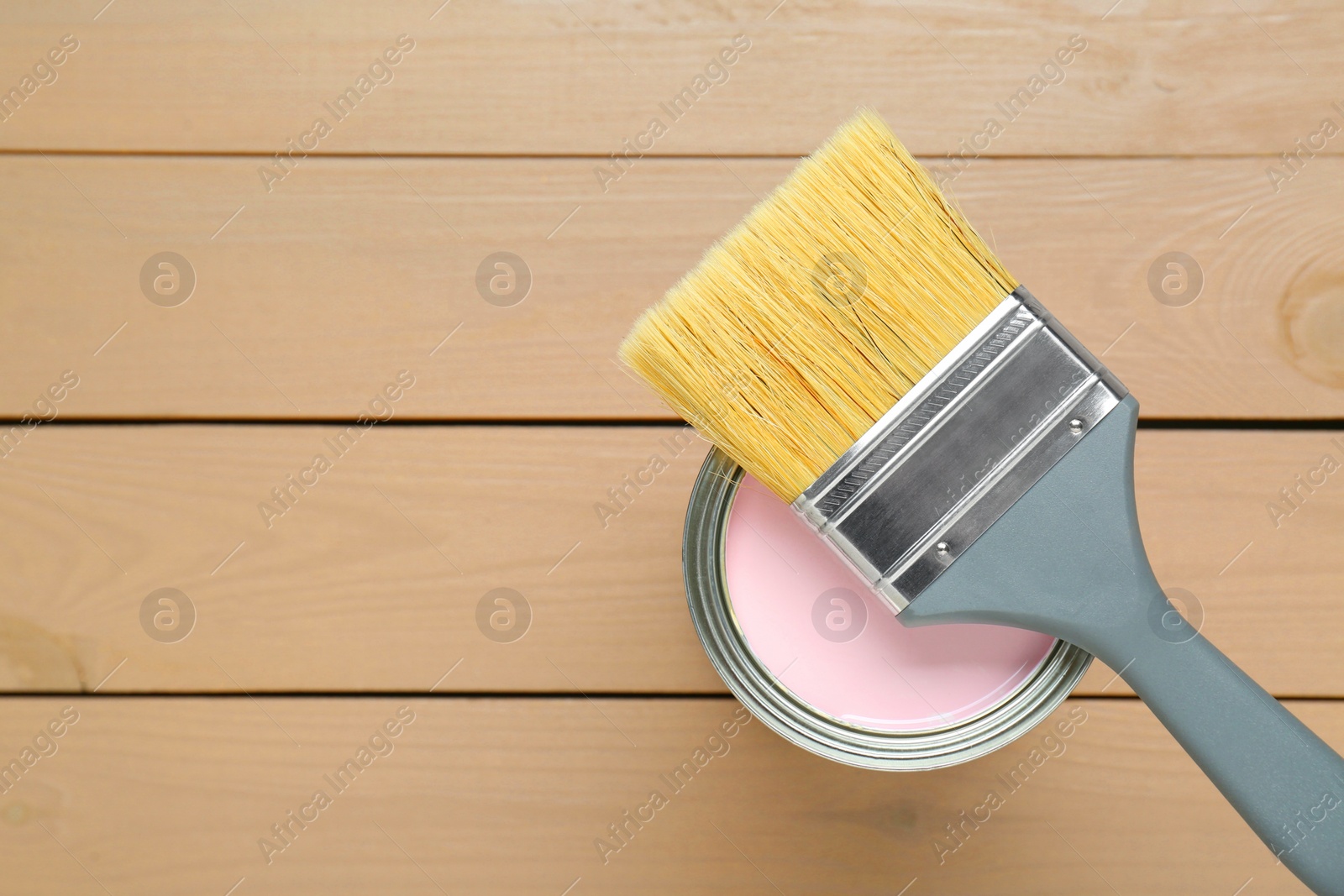 Photo of Can of pale pink paint with brush on wooden table, top view. Space for text