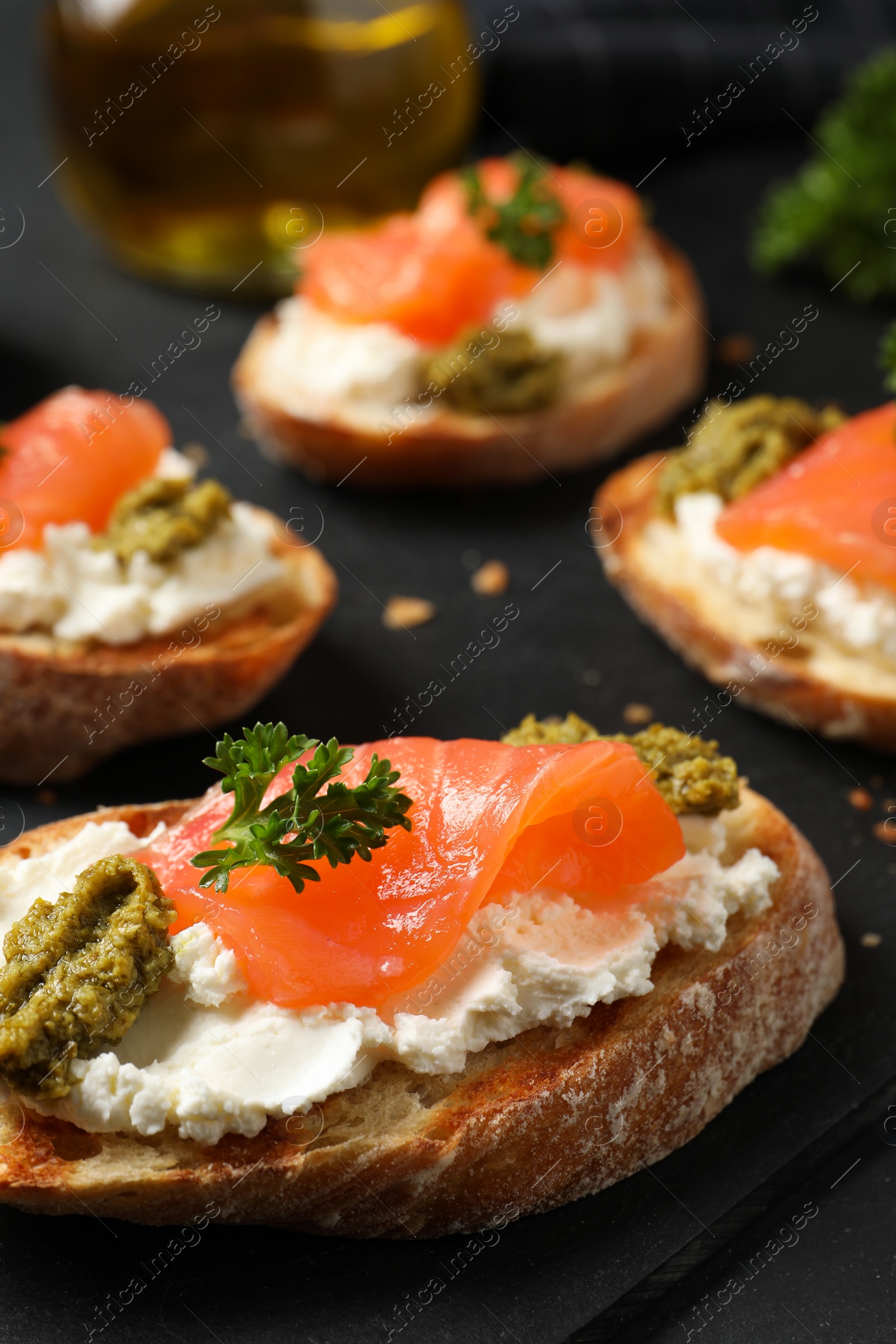 Photo of Delicious bruschettas with cream cheese, salmon and pesto sauce on black table, closeup