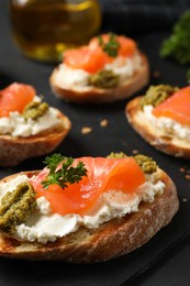 Photo of Delicious bruschettas with cream cheese, salmon and pesto sauce on black table, closeup