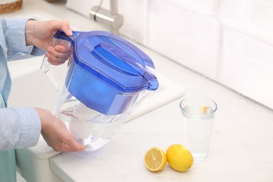 Photo of Woman with water filter jug in kitchen, closeup