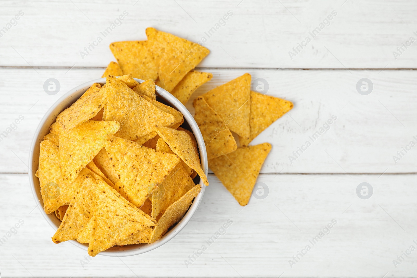 Photo of Bowl and tasty Mexican nachos chips on white wooden table, flat lay. Space for text