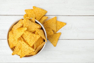 Photo of Bowl and tasty Mexican nachos chips on white wooden table, flat lay. Space for text
