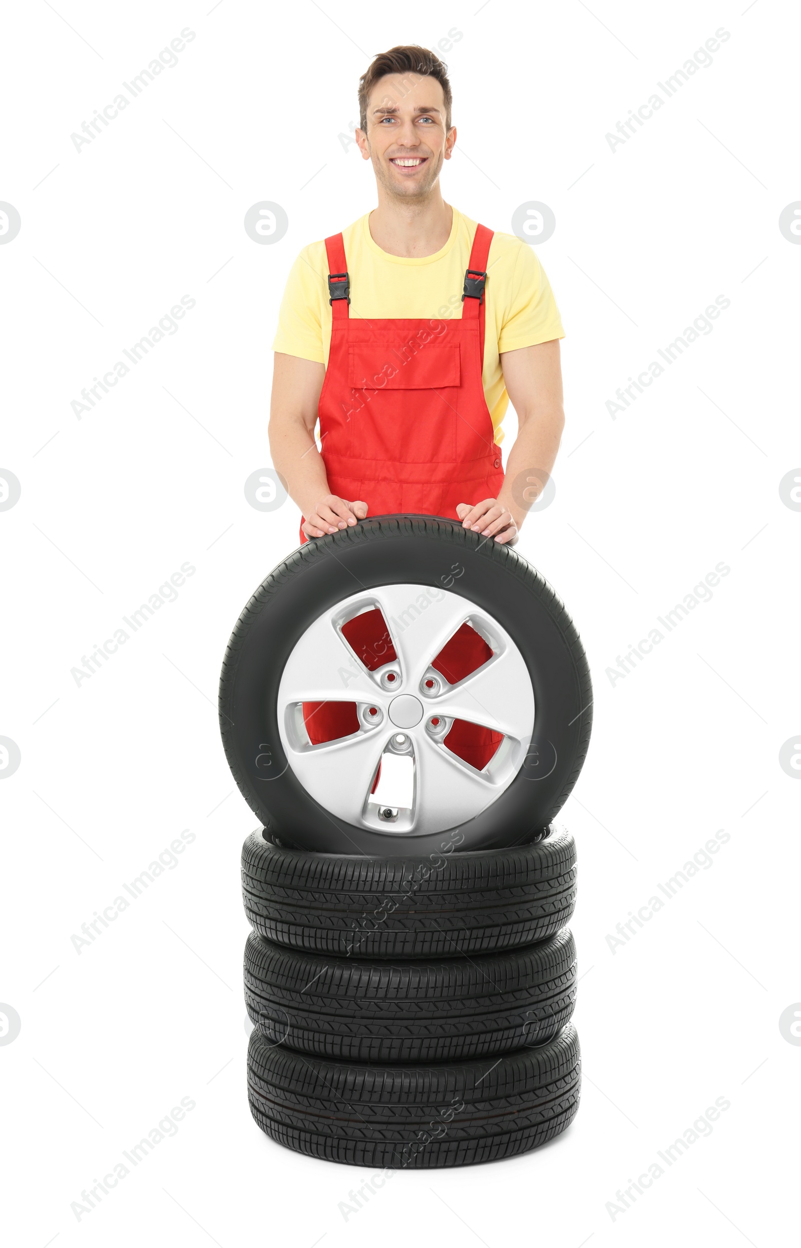 Photo of Young mechanic in uniform with car tires on white background