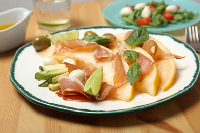 Photo of Plate with melon and prosciutto appetizer on wooden table