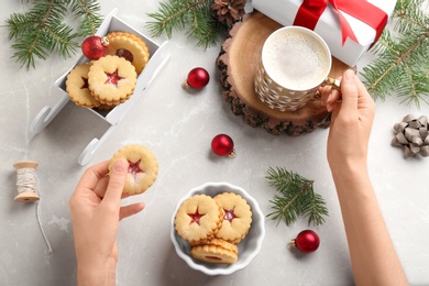 Woman eating traditional Christmas Linzer cookies with sweet jam at table, top view