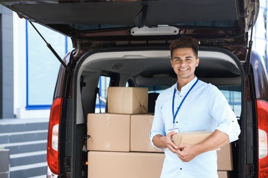 Photo of Young courier with parcel near delivery car outdoors