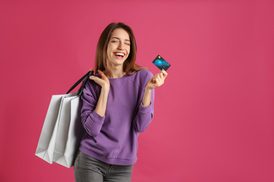 Photo of Happy young woman with credit card and shopping bags on pink background, space for text. Spending money
