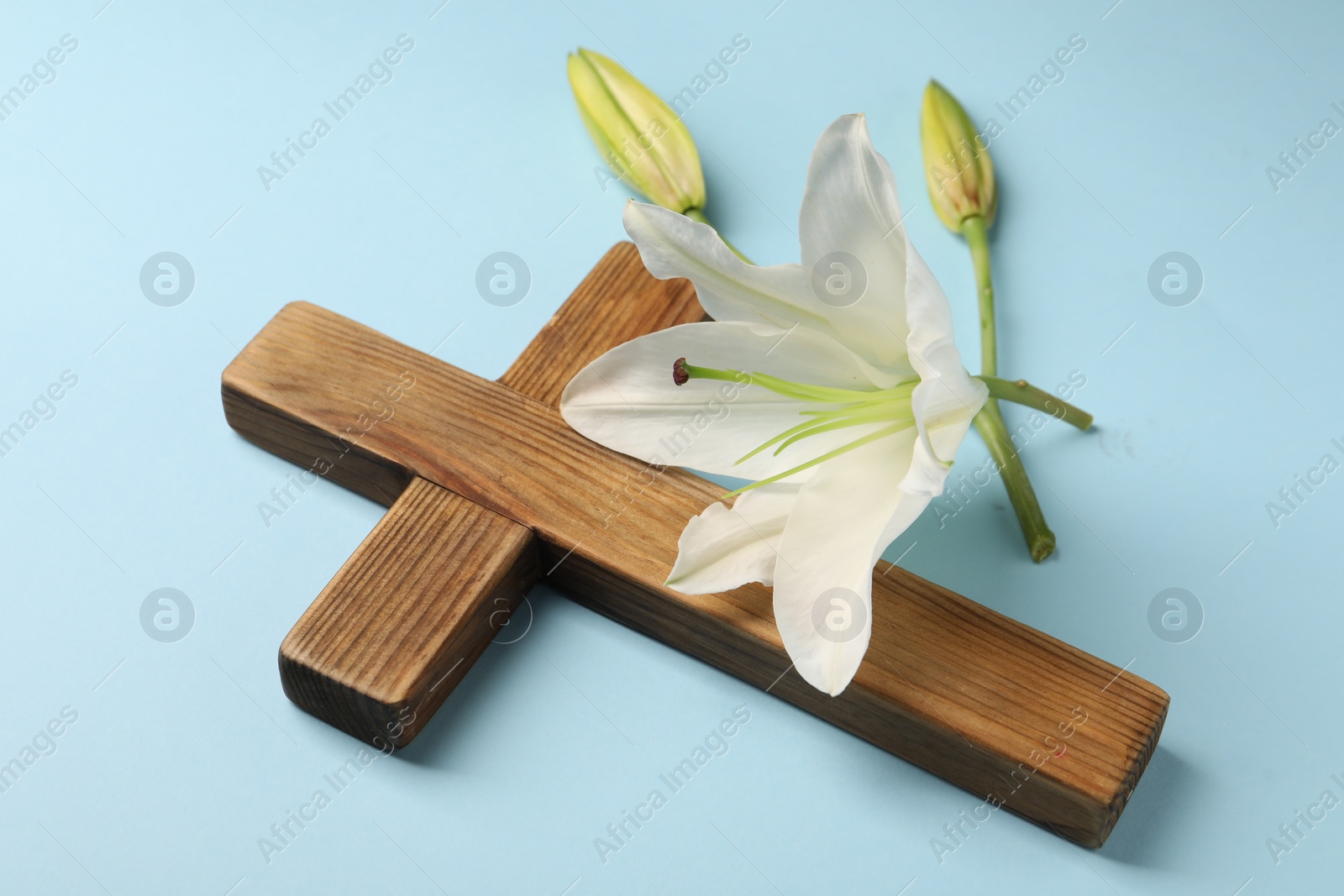 Photo of Wooden cross and lily flowers on light blue background. Easter attributes