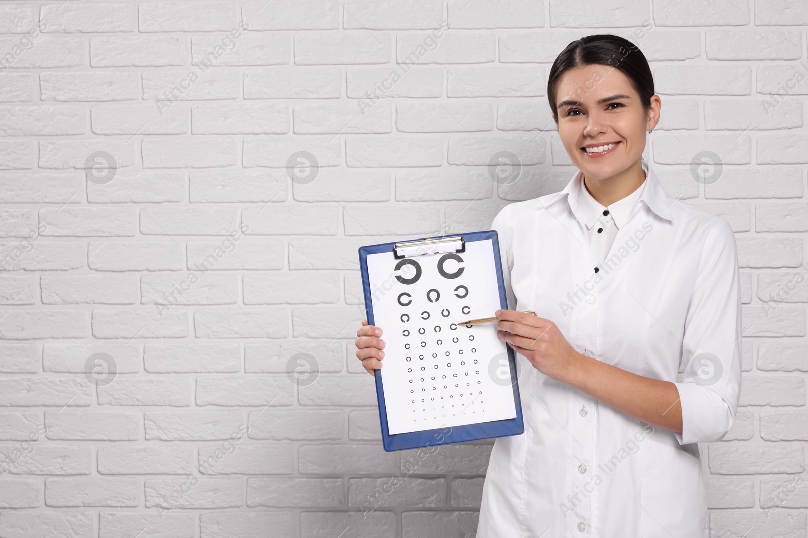 Photo of Ophthalmologist pointing at vision test chart near white brick wall, space for text