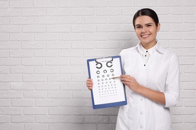 Ophthalmologist pointing at vision test chart near white brick wall, space for text