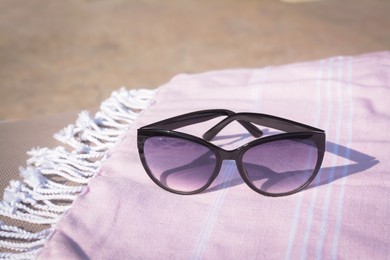 Stylish sunglasses on blanket outdoors, closeup. Beach accessories