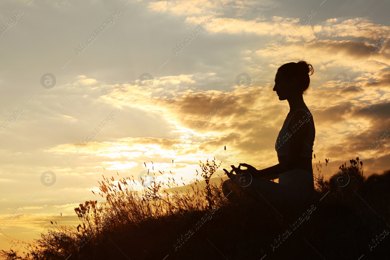 Photo of Silhouette of woman meditating outdoors at sunset. Space for text