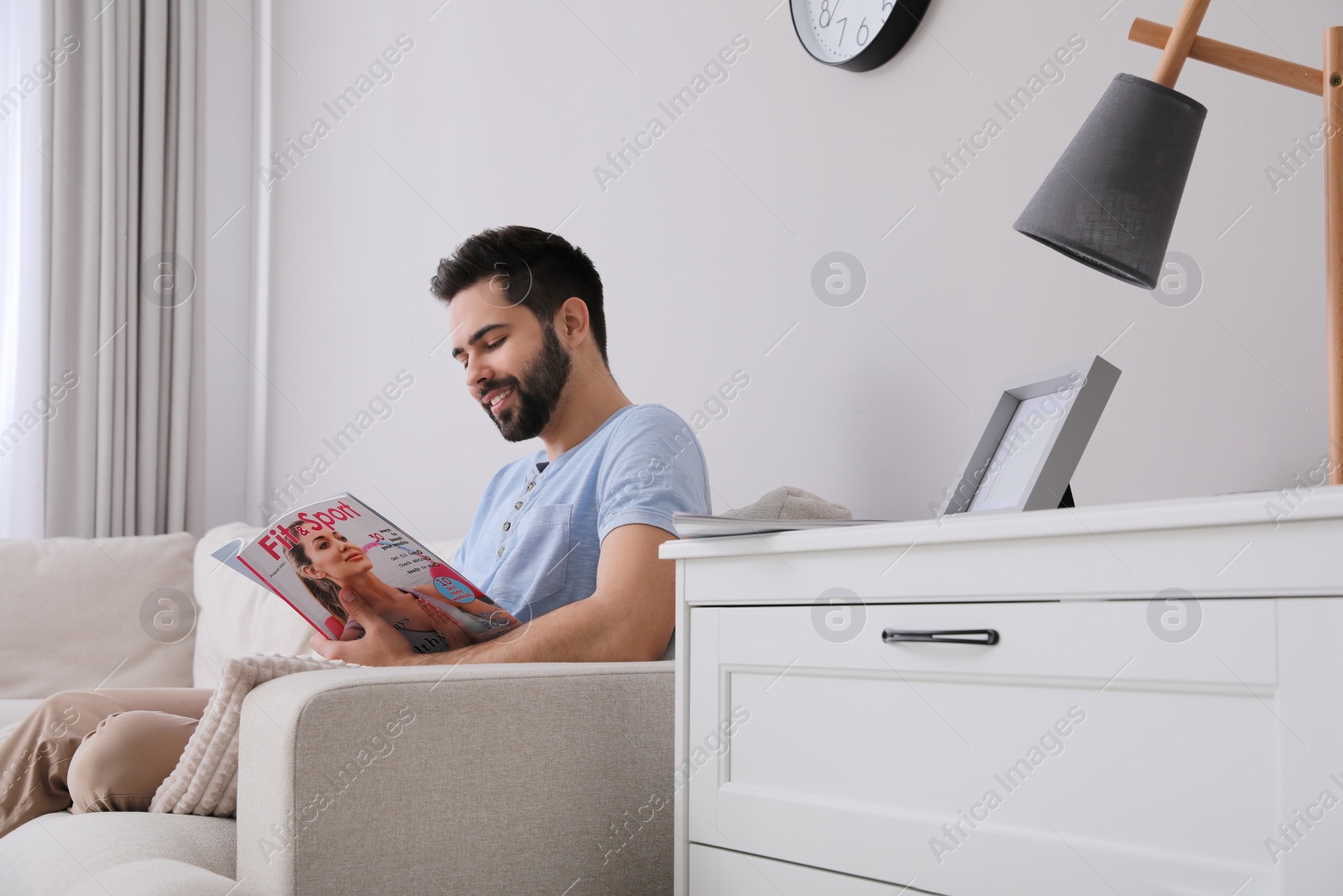Photo of Young man reading sports magazine on sofa at home