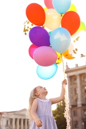 Cute little girl with colorful balloons outdoors on sunny day