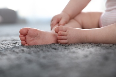 Photo of Barefoot little child with sitting on grey carpet indoors, closeup