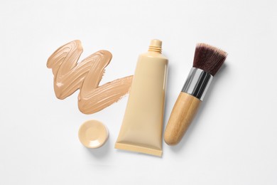 Photo of Liquid foundation, makeup brush and swatch on white background, flat lay