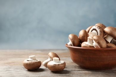 Photo of Fresh champignon mushrooms and bowl on wooden table, space for text
